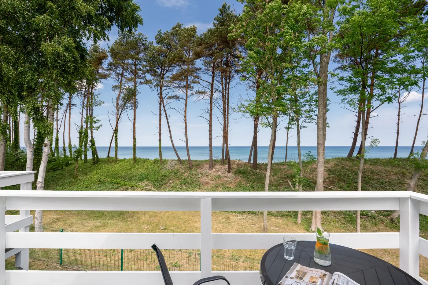 Balkon domku letniskowego w Sarbinowie ze stolikiem i widokiem na morze przez sosny