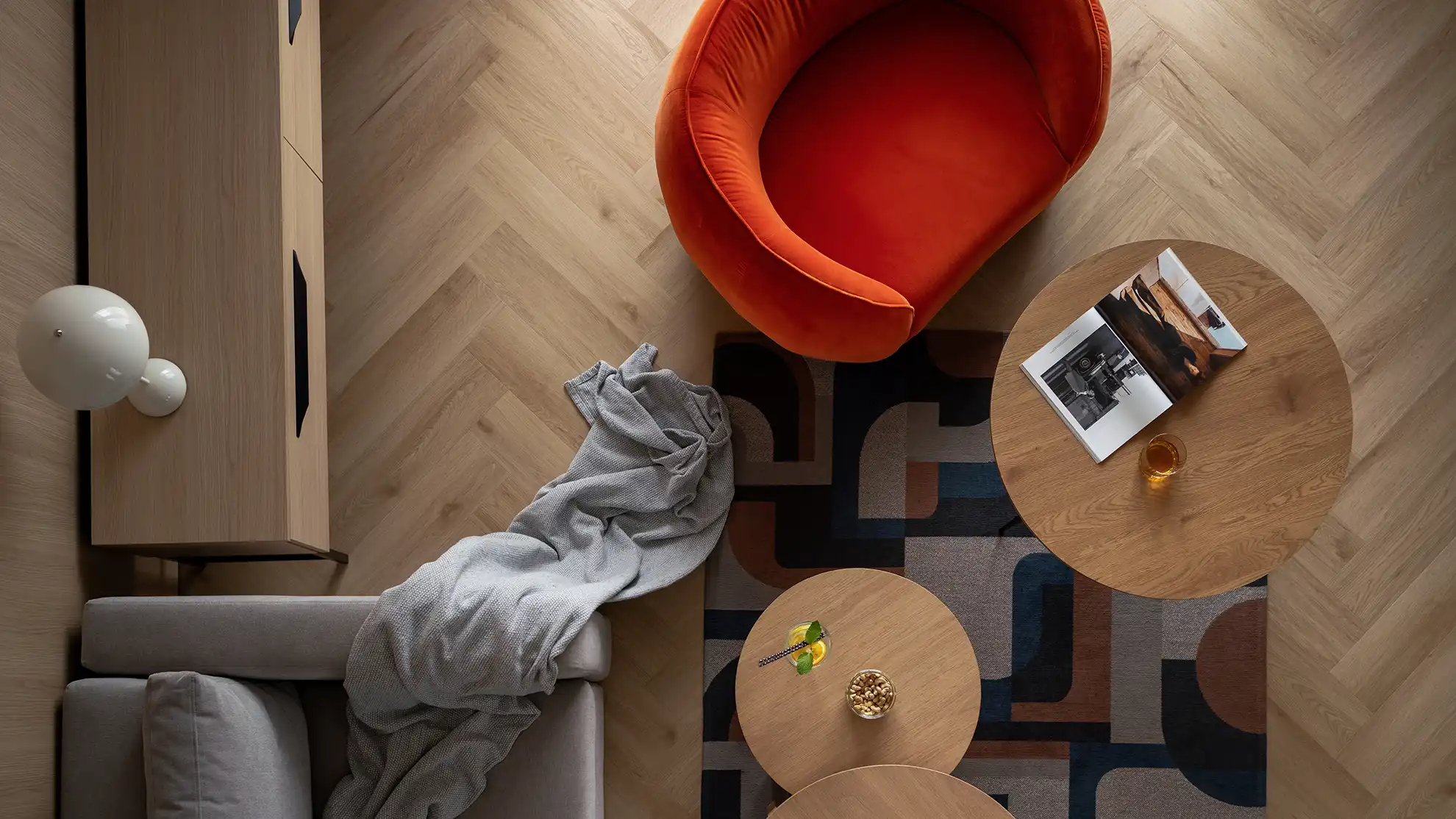 Wnętrze apartamentu z czerwonym fotelem i drewnianą podłogą w jodełkę, widziane z góry