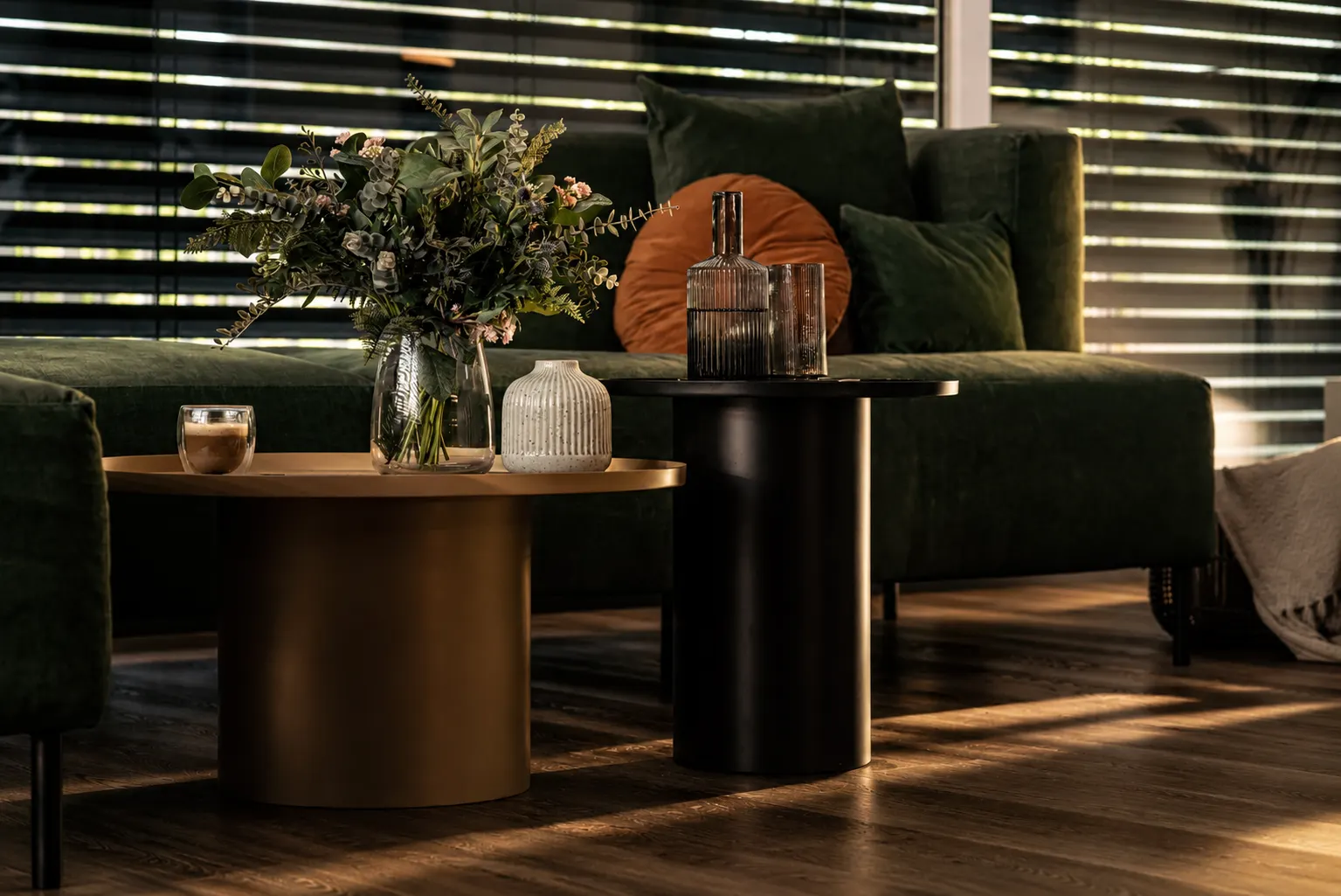 Zielona sofa, okrągłe stoliki i bukiet w świetle przechodzącym przez żaluzje