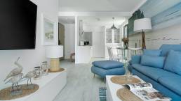 Jasny salon apartamentu Sea & Forest z dużymi przeszkleniami, naturalnym światłem i błękitnymi akcentami – fotografia wnętrz premium Międzyzdroje